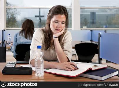 Young woman studying in a library, absently staring at her books