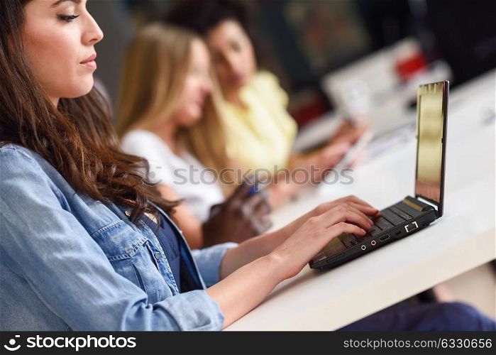 Young woman studying with laptop computer on white desk. Beautiful girls and guys working together wearing casual clothes. Multi-ethnic coworkers group.