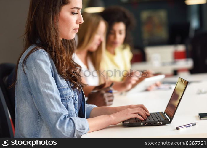 Young woman studying with laptop computer on white desk. Beautiful girls and guys working together wearing casual clothes. Multi-ethnic coworkers group.