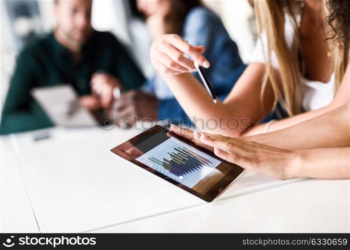 Young woman studying with tablet computer on white desk. Beautiful girls and guys working together wearing casual clothes. Coworkers group.