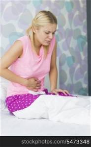 Young woman suffering from abdomen pain in bedroom