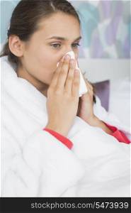 Young woman suffering from cold blowing nose in bedroom