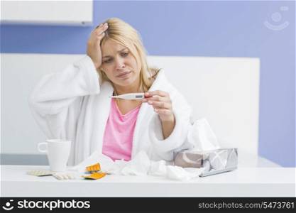 Young woman suffering from cold checking tempereature