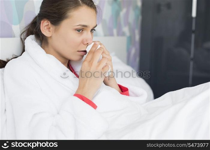 Young woman suffering from cold using tissue paper in bedroom