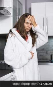 Young woman suffering from headache standing in kitchen