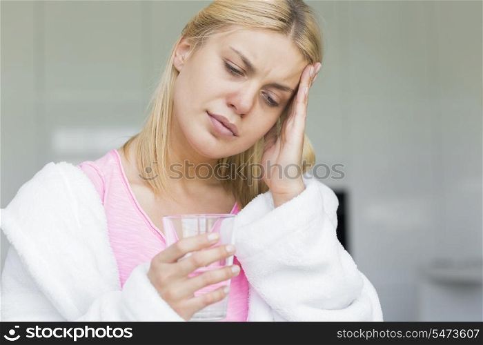 Young woman suffering from headache while holding glass of water