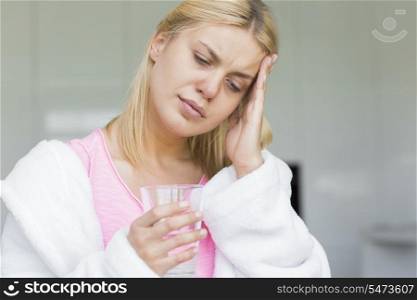 Young woman suffering from headache while holding glass of water