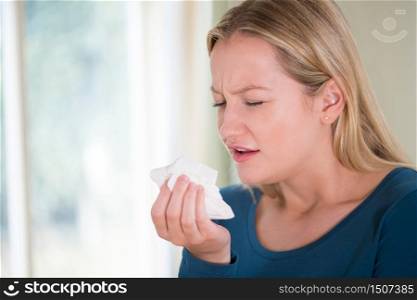 Young Woman Suffering With Cold Sneezing Into Tissue