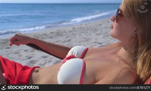 Young woman sunbathing in lounge chair on summer sandy beach