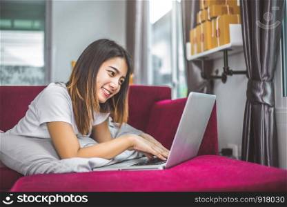 Young woman surfing the internet by laptop on red sofa in cheerful gesture mood emotion. Selling and online shopping concept. Merchant and marketing. Happiness of new business trader and entrepreneur