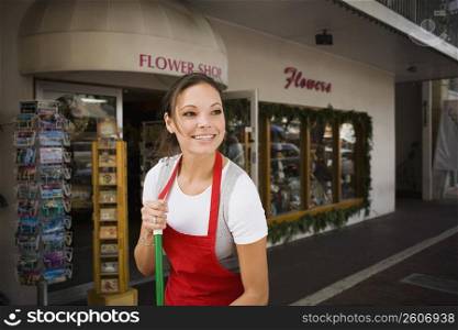 Young woman sweeps outside flower shop
