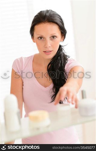 Young woman take beauty care product from bathroom shelf