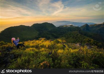 young woman take photographs during Sunset on mountain with landscape view