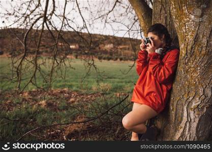 Young woman taking a photo with old camera wear a red raincoat on field in a rainy day