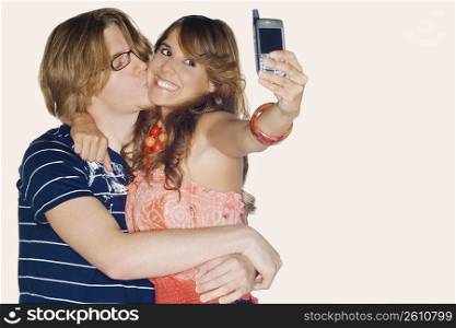 Young woman taking a photograph of herself with a young man kissing her