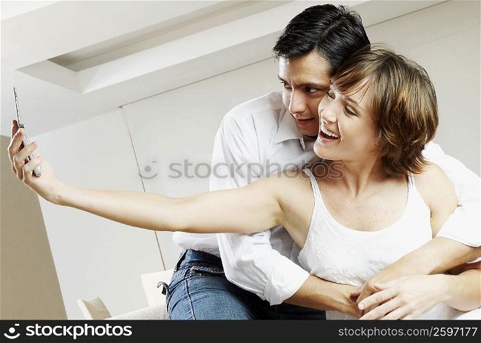 Young woman taking a picture with a mid adult man embracing her from behind
