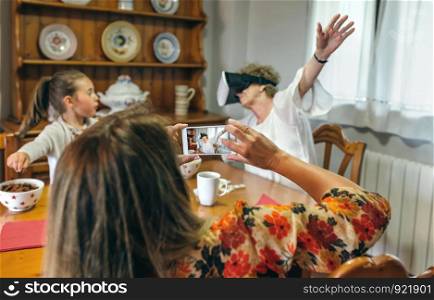 Young woman taking a picture with the mobile phone to her mother using a virtual reality glasses. Selective focus on smartphone in foreground.. Young woman taking a picture to her mother using virtual reality glasses