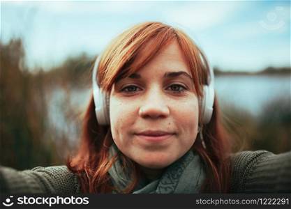 Young woman taking a selfie with her smartphone near a lake and headphones
