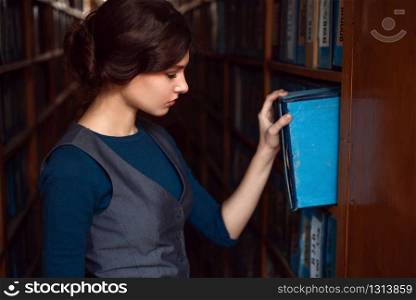 Young woman taking book from library shelf. Knowledge, education and studying concept.