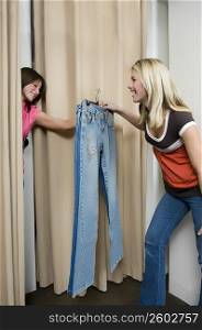 Young woman taking jeans from a sales clerk in a fitting room