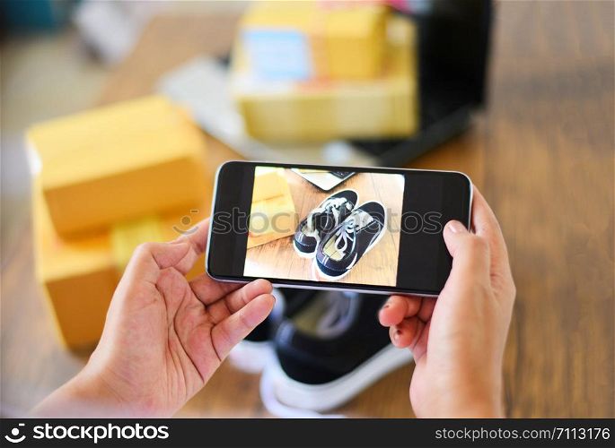 young woman taking photo sneakers with camera smartphone for post to sell online on the internet market website / selling online ecommerce shipping online shopping delivery and order concept