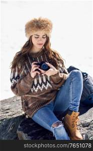 Young woman taking photographs in the snowy mountains in winter, in Sierra Nevada, Granada, Spain. Female wearing winter clothes.. Young woman taking photographs in the snowy mountains