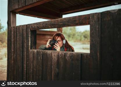 Young woman taking photos from wooden hut in the forest