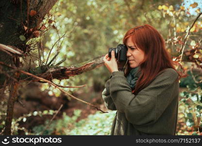 Young woman taking photos in the forest with an old analog camera