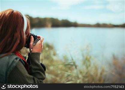 Young woman taking photos in the forest with an old analog camera and headphones