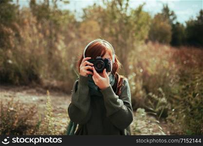Young woman taking photos in the forest with an old analog camera and headphones