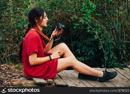 Young woman taking photos in the forest with her analogical camera wearing a red mini dress.