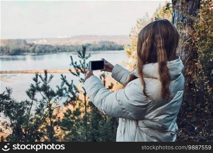 Young woman taking photos of landscape with her smartphone during trip on autumn sunny day. Young woman taking photos of landscape with smartphone