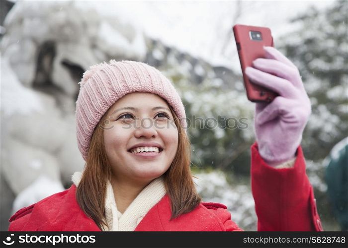 Young woman taking picture with cell phone in snow