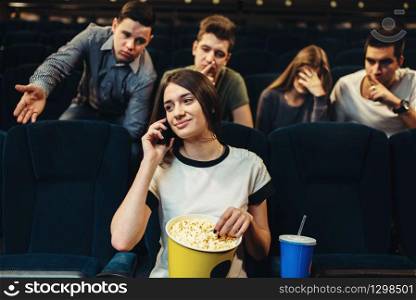 Young woman talking by phone in cinema, audience dissatisfied. Showtime, movie watching