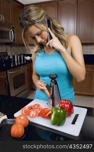 Young woman talking on a mobile phone and grating a carrot in the kitchen