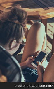 Young woman talking on a mobile phone sitting in a chair outdoors on patio wearing a sunglasses. Real people, authentic situations