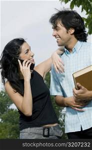 Young woman talking on a mobile phone with a young man standing beside her