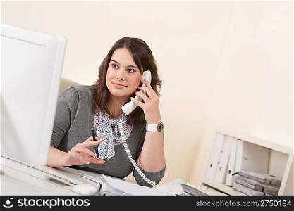 Young woman talking on the phone at office by computer