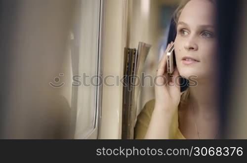 Young woman talking on the phone in the train and looking out the window.