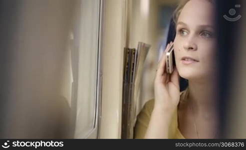 Young woman talking on the phone in the train and looking out the window.