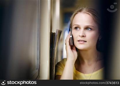 Young woman talking on the phone in the train and looking out the window.