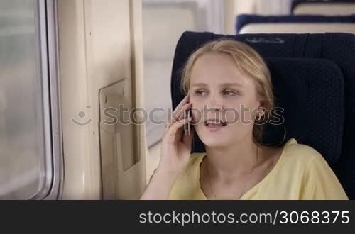 Young woman talking on the phone in the train while looking out the window.
