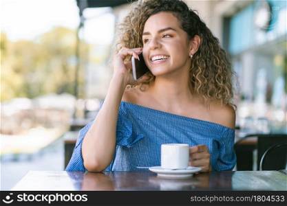 Young woman talking on the phone while drinking a cup of coffee at a coffee shop.