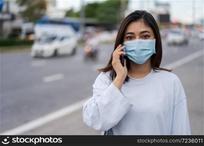 young woman talking with mobile phone in city street and wearing face mask protective for spreading of coronavirus(covid-19) pandemic, new normal concept
