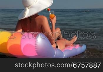 young woman tanning on the beach with a cocktail in hand