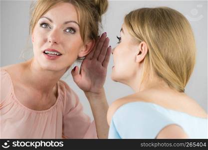Young woman telling her friend some secrets, two women talking gossiping. Excited emotional girl whispering to ear. Two teen women gossiping