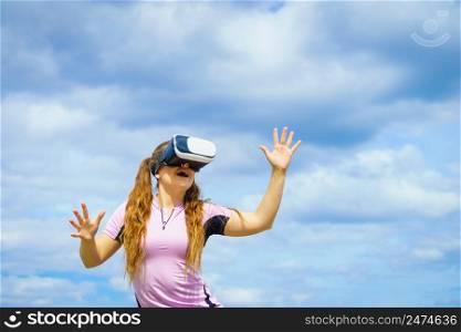 Young woman testing VR glasses outside. Female wearing virtual reality headset during summer weather. Woman wearing VR outside