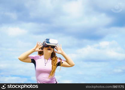 Young woman testing VR glasses outside. Female wearing virtual reality headset during summer weather. Woman wearing VR outside