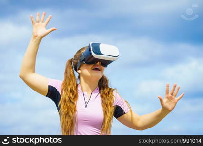 Young woman testing VR glasses outside. Female wearing virtual reality headset during summer weather. Woman wearing VR outside