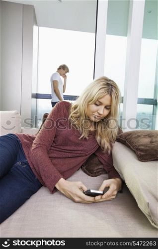 Young woman text messaging while man using cell phone in background at home